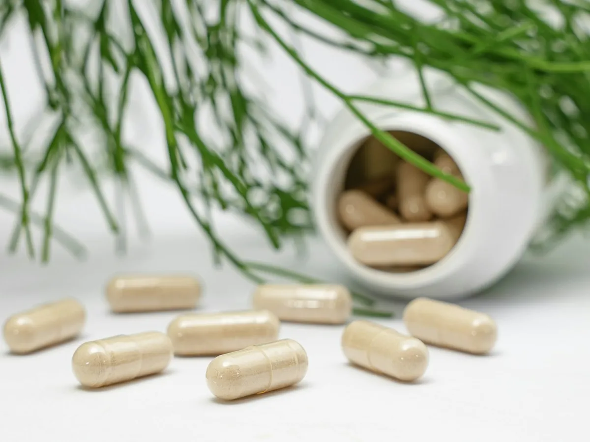 Capsules naast een open potje, met groene twijgjes
