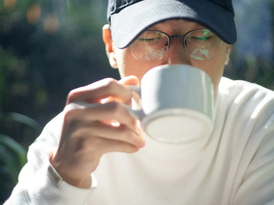 Oudere man met pet drinkt uit een beker