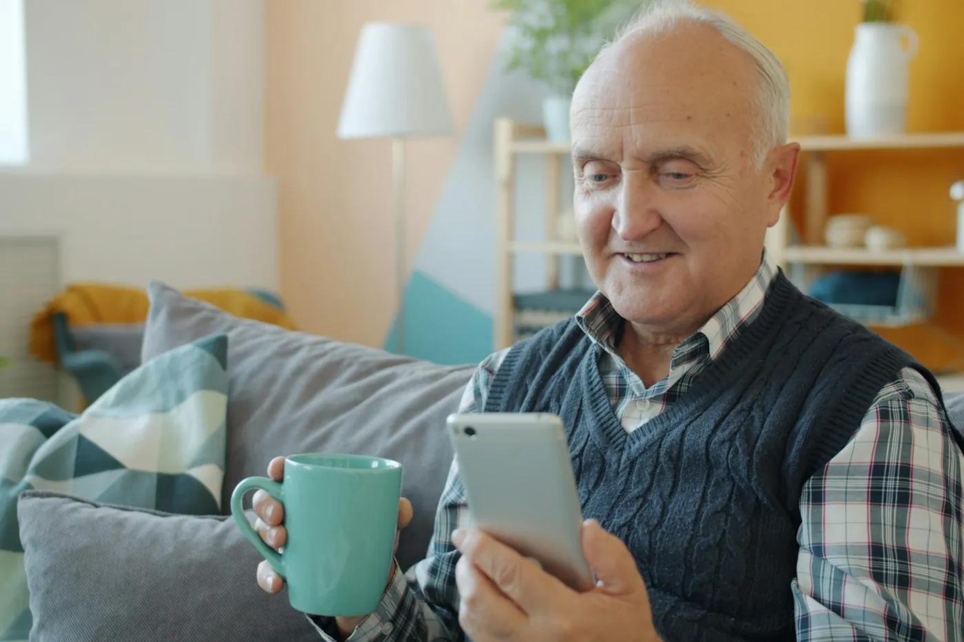 Oudere man met een mok en zijn telefoon op de bank